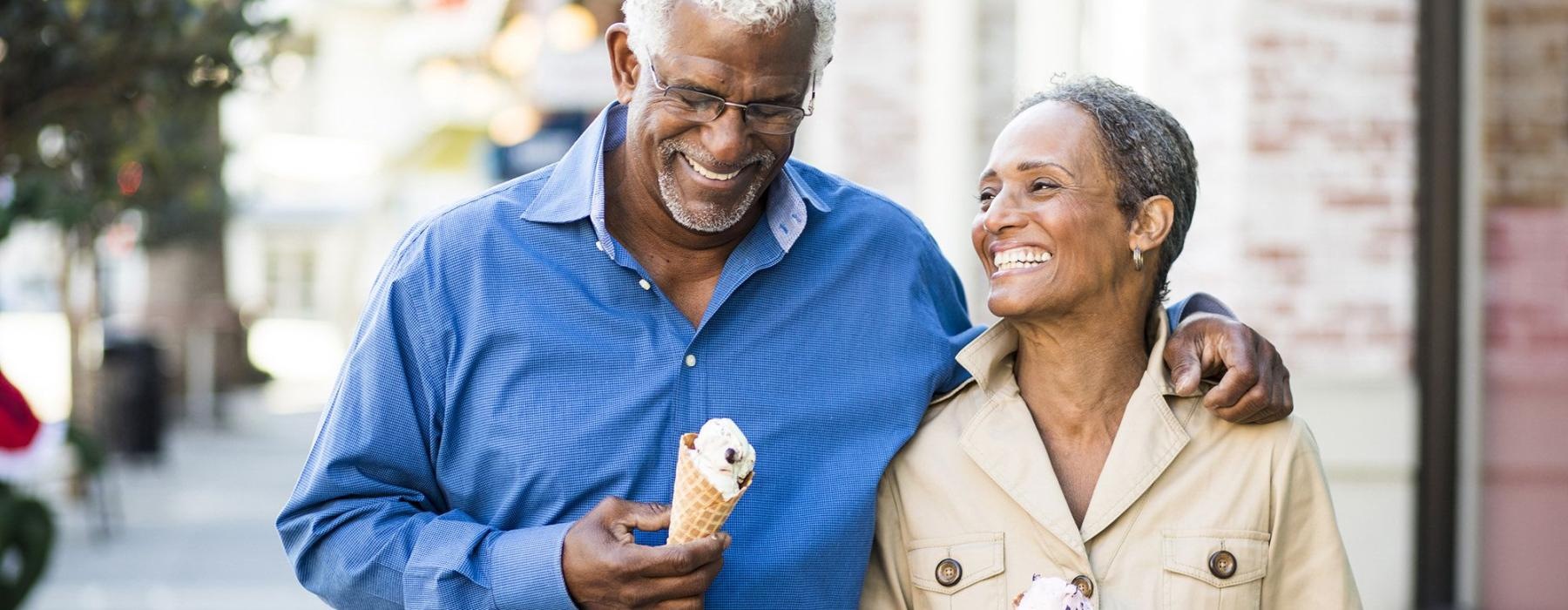 older couple walks down city sidewalk while holding ice cream cones