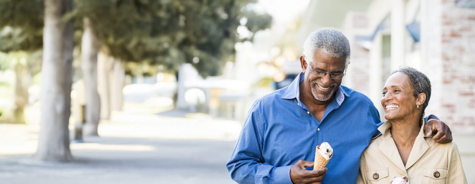 older couple walks down city sidewalk while holding ice cream cones